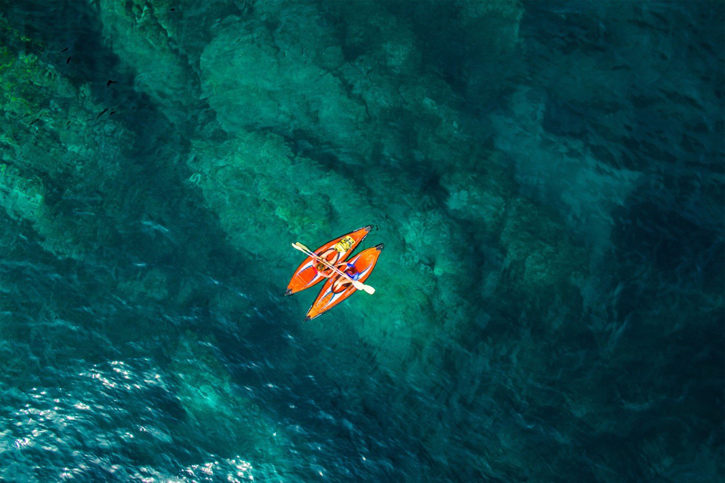 A person in an orange kayak floating on top of the ocean.